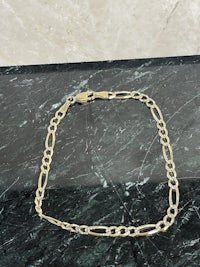 a gold figaro chain bracelet on a marble table