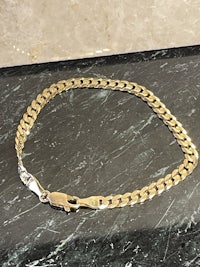 a gold chain bracelet sitting on a marble table